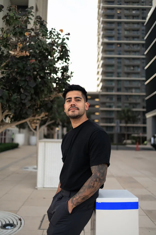 A man outdoors in a black t-shirt and black trousers, with towers behind him