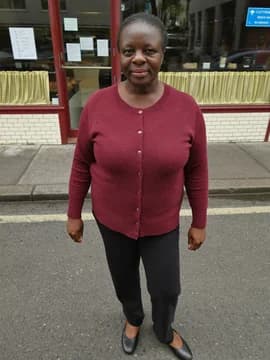 A woman outside a bakery in a burgundy cardigan and black trousers