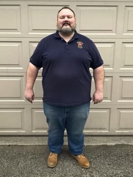 A bearded man by a garage door in a navy polo shirt and jeans